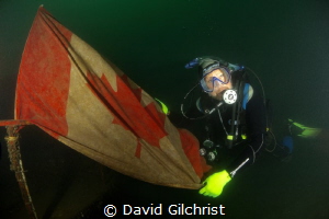 Diver unfurls the flag at the bow of sunken boat in the W... by David Gilchrist 